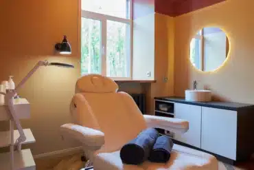 Interior of the cosmetology office with a sink, a round mirror, an electrical facial beauty bed and chair.