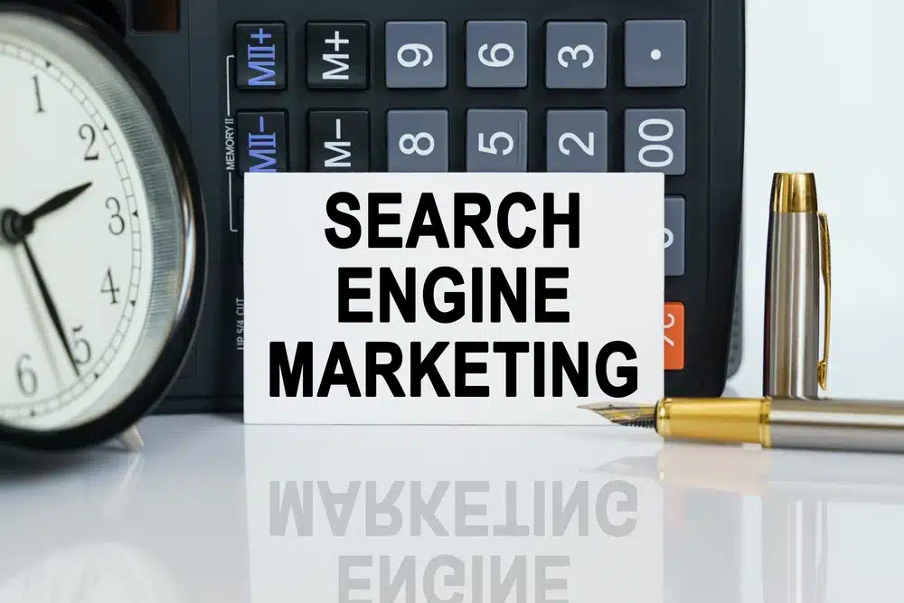 clock, a pen, a calculator and a business card on which the text is written: SEARCH ENGINE MARKETING